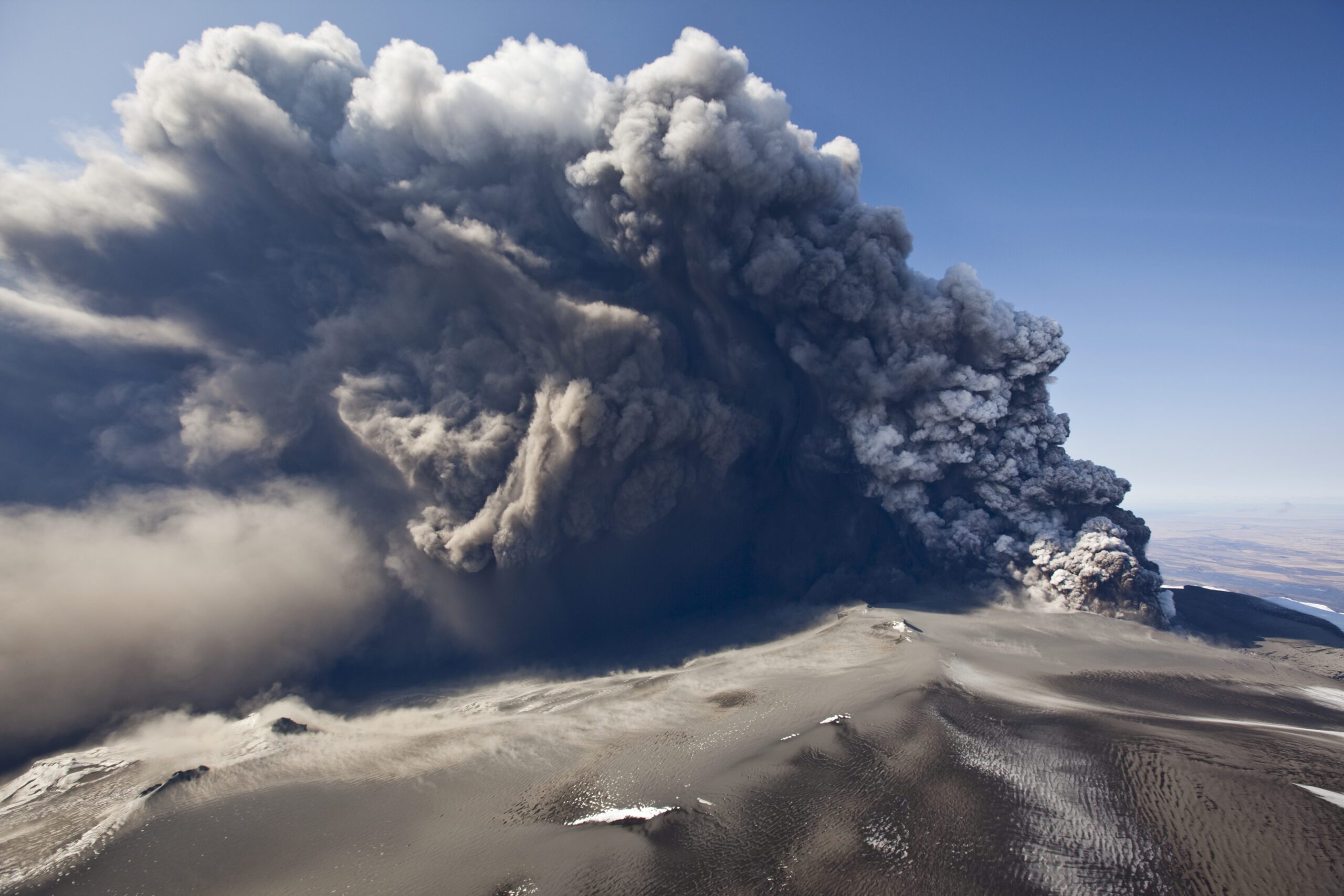 Aerial view of a volcano spewing a large ash cloud into the air