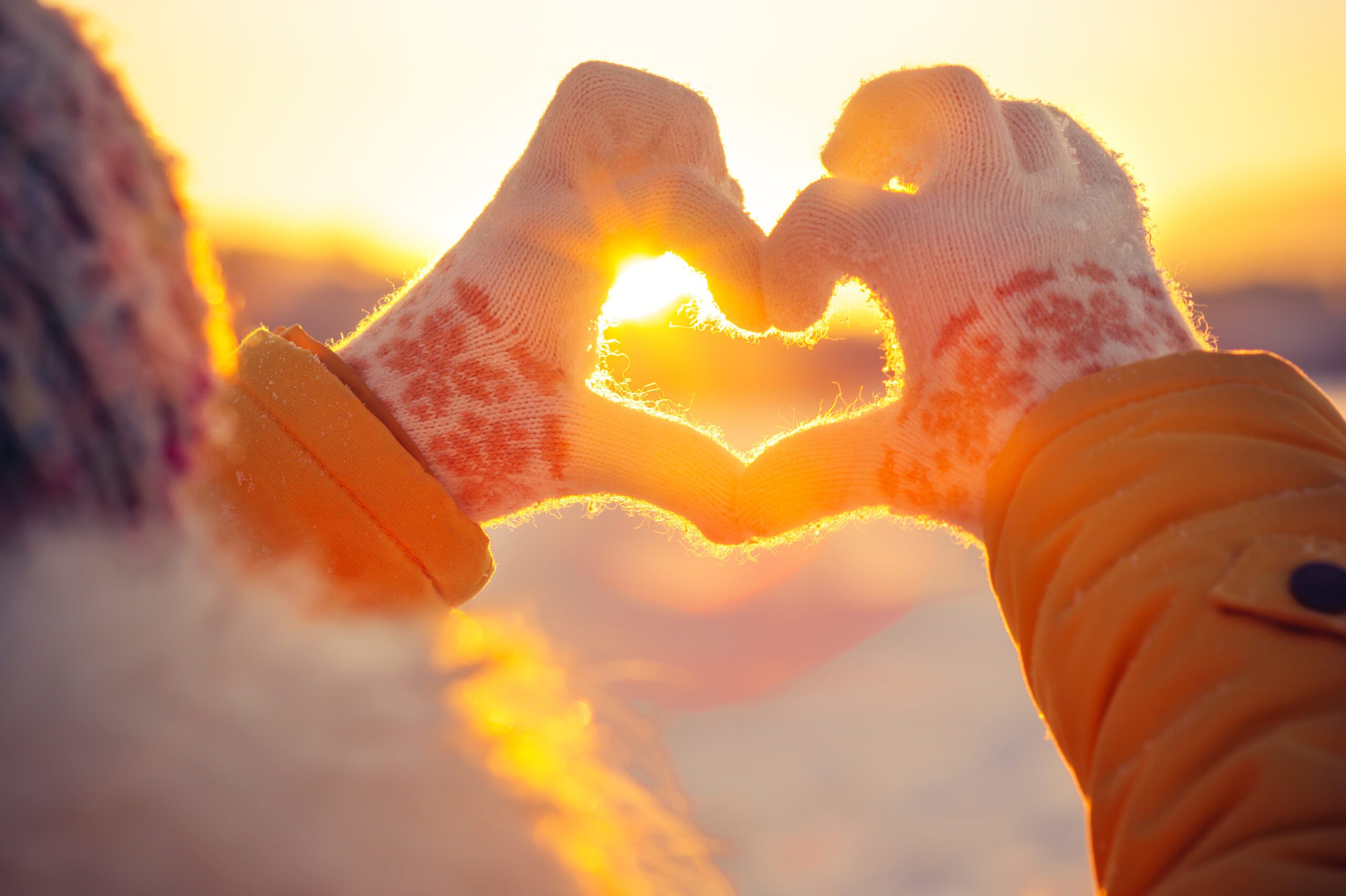 A woman making a heart symbol with her hands outdoors in the winter.