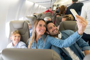 Happy family traveling by plane and taking a selfie with a cell phone while smiling - travel concepts